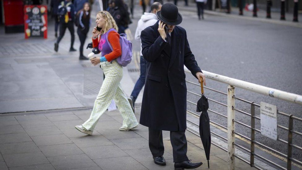 A person wearing bowler hat walks in the City of London