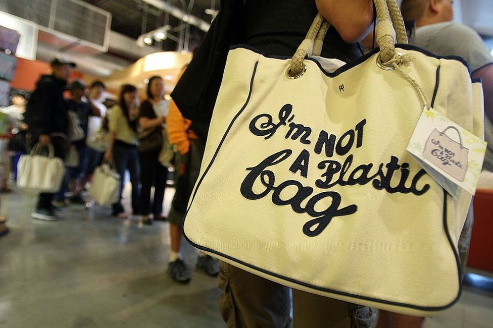 A customer holds a shopping bag designed by Anya Hindmarch which reads 'I'm Not a Plastic Bag'