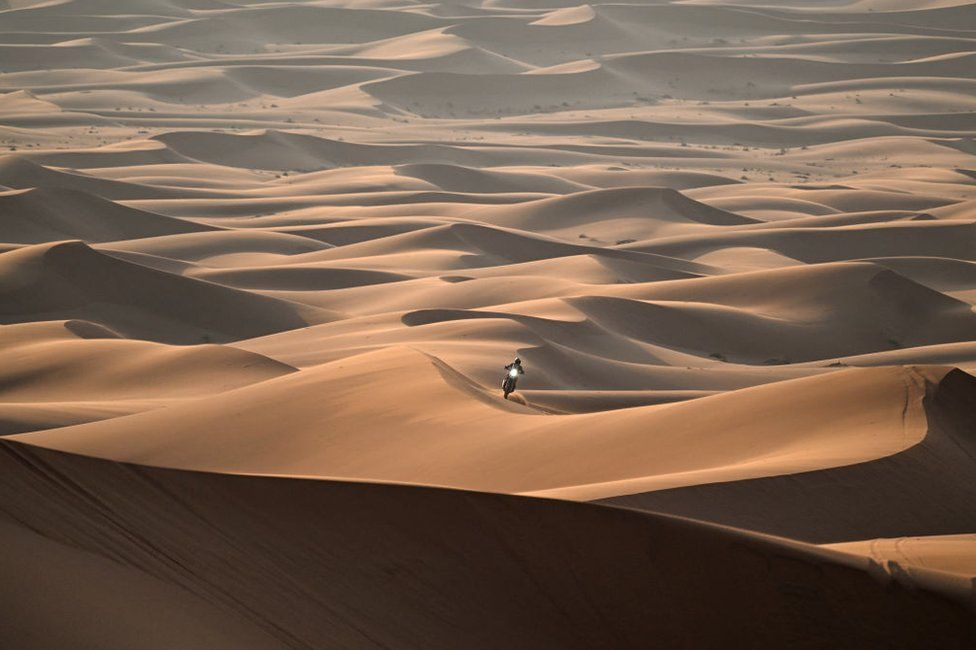A man rides a motorbike over sand dunes.