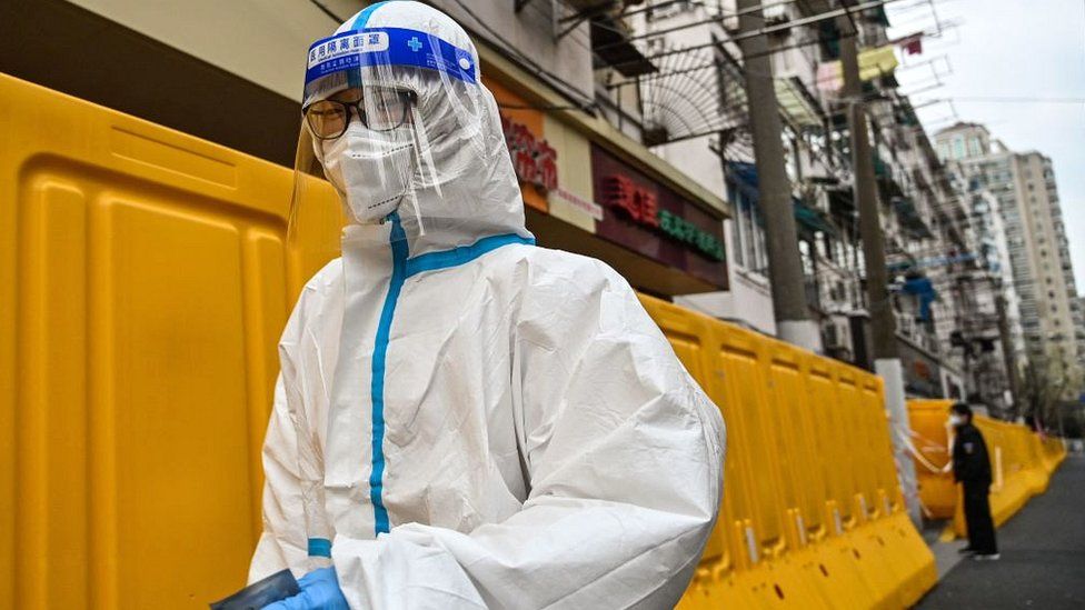 A worker, wearing a protective gear, walks next to barriers that separate the street and a neighbourhood in lockdown in Shanghai.