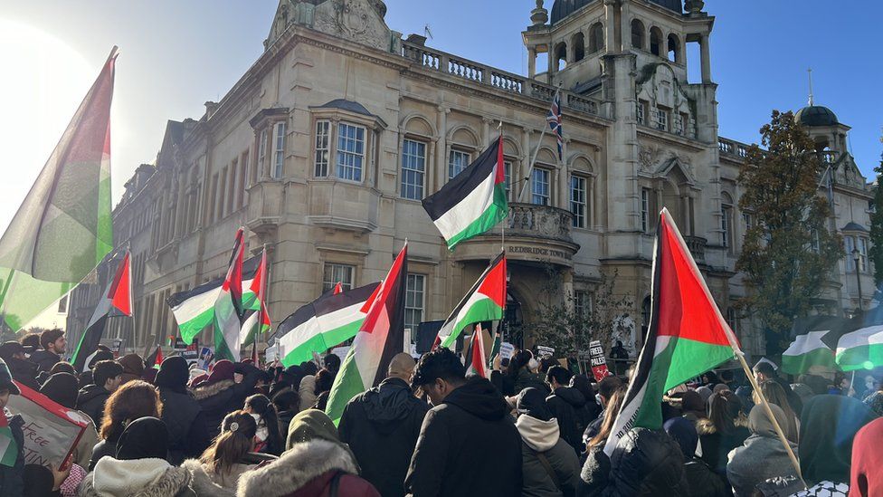 A protest in Ilford involving school children, with people waving Palestinian flags.
