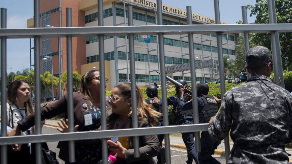 Сотрудники министерства окружающей среды Доминиканы пытаются выбраться из ворот штаб-квартиры министерства во время стрельбы в Санто-Доминго 6 июня 2022 года. Министр окружающей среды Доминиканы Орландо Хорхе Мера был застрелен в своем офисе в понедельник.
