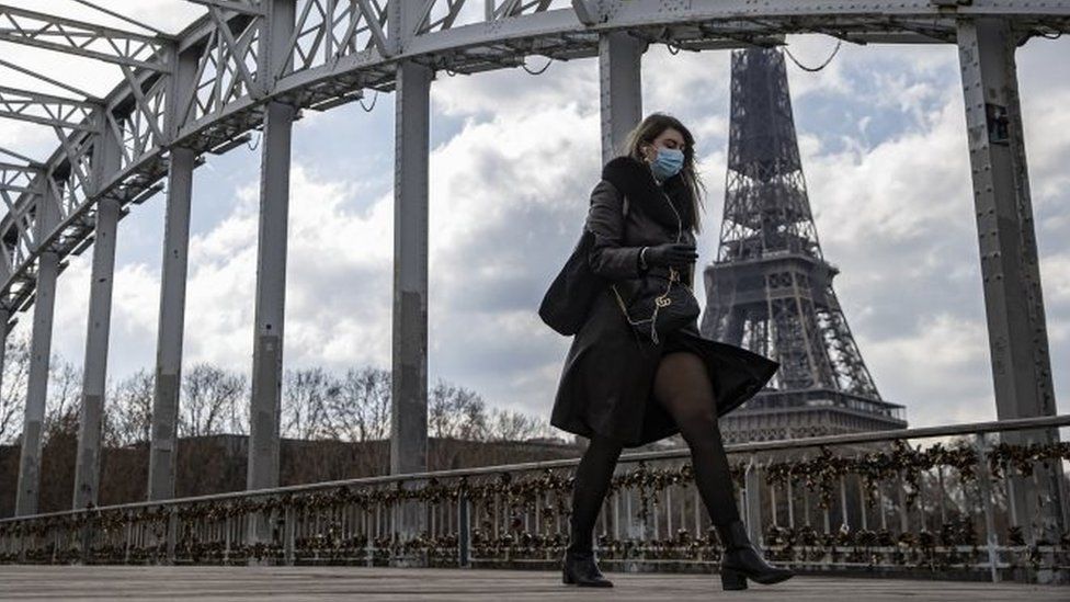 Женщина в маске идет по пешеходному мосту возле Эйфелевой башни в Париже, Франция. Фото: 19 марта 2021 г.