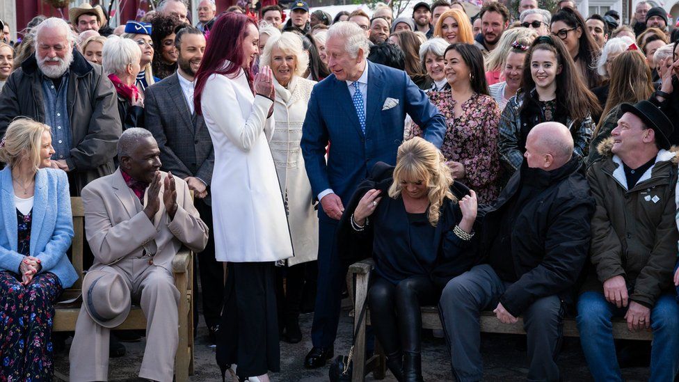 The Prince of Wales lends Letitia Dean his coat during a visit to the set of EastEnders