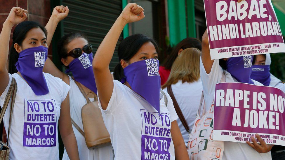 Female anti-Duterte campaigners stand with fists raised, wearing T-shirts reading "No to Duterte. No to rape."