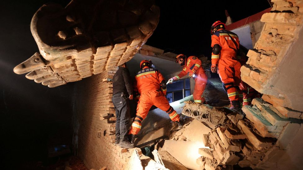 Rescuers in orange outfits climb through damaged buildings in Kangdiao village in Jishishan county