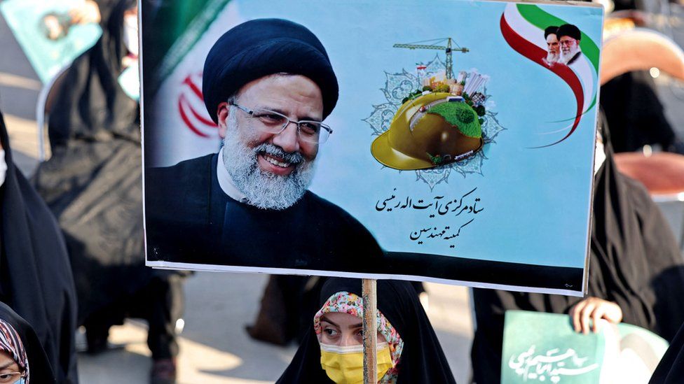 Женщина в головном платке и маске держит плакат с изображением Эбрахима Раиси, когда она присутствует на митинге предвыборной кампании в столице Тегеране 14 июня 2021 г.