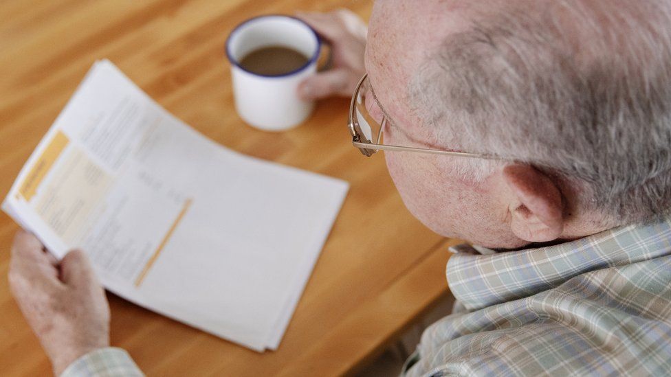 A man looks at his energy bills while drinking something from a mug