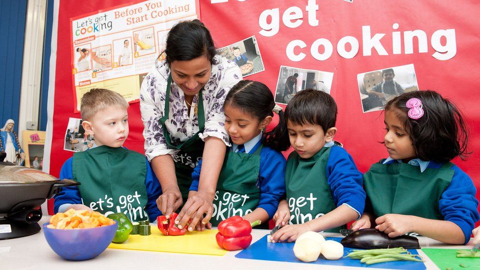 A woman showing four children how to chop red peppers