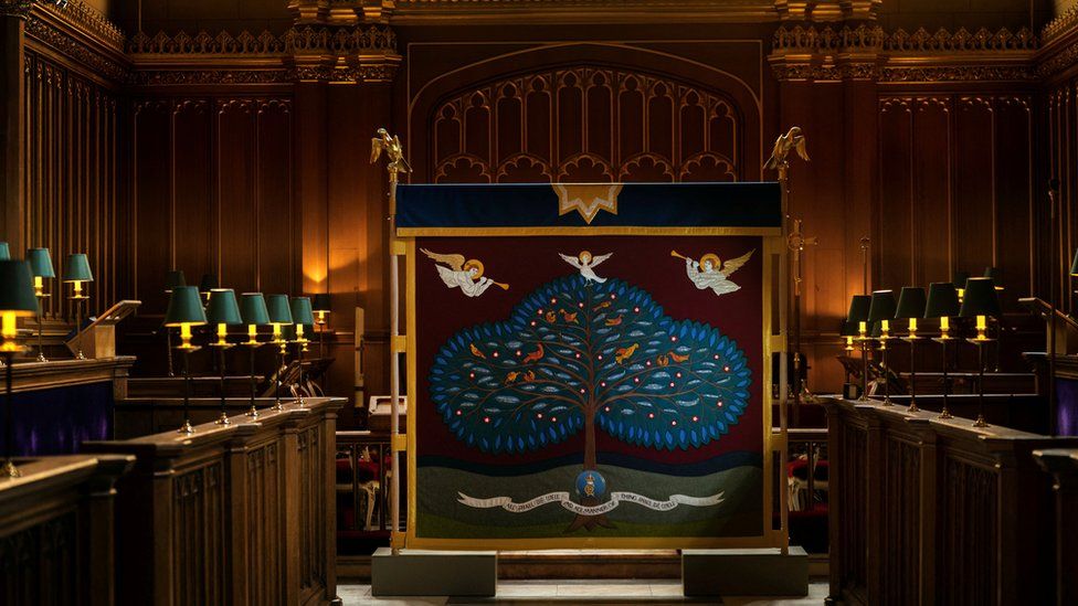 An embroidered cloth screen is decorated with a large tree which represents the 56 member countries of the Commonwealth and three angels flying above it.