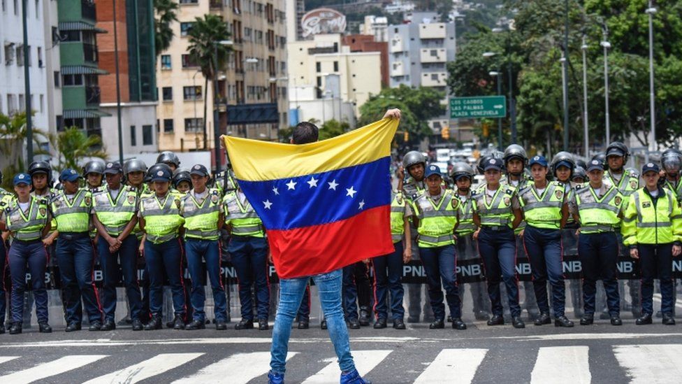 A member of the Venezuela"s opposition gestures showing a national flag in front of National policemen during a demonstration in Caracas on July 27, 2016.