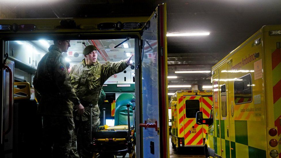 Military personnel stand inside the back of an ambulance alongside equipment, at the barracks.