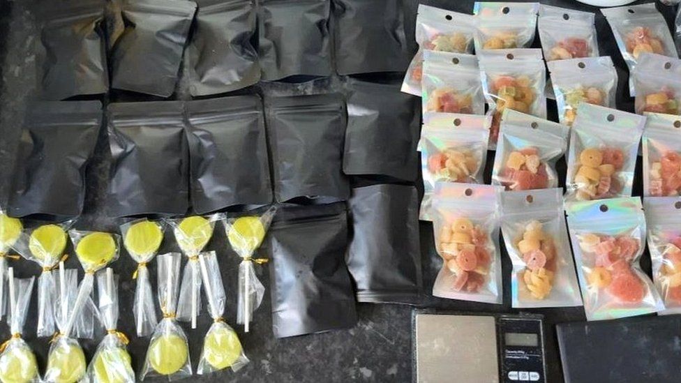 Yellow cannabis lollies and bags of red and orange cannabis sweets laid out on a counter