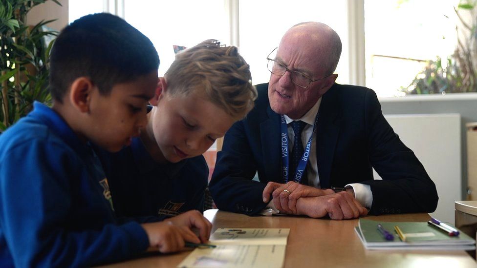 Schools minister Nick Gibb with two pupils reading at a school in Wakefield