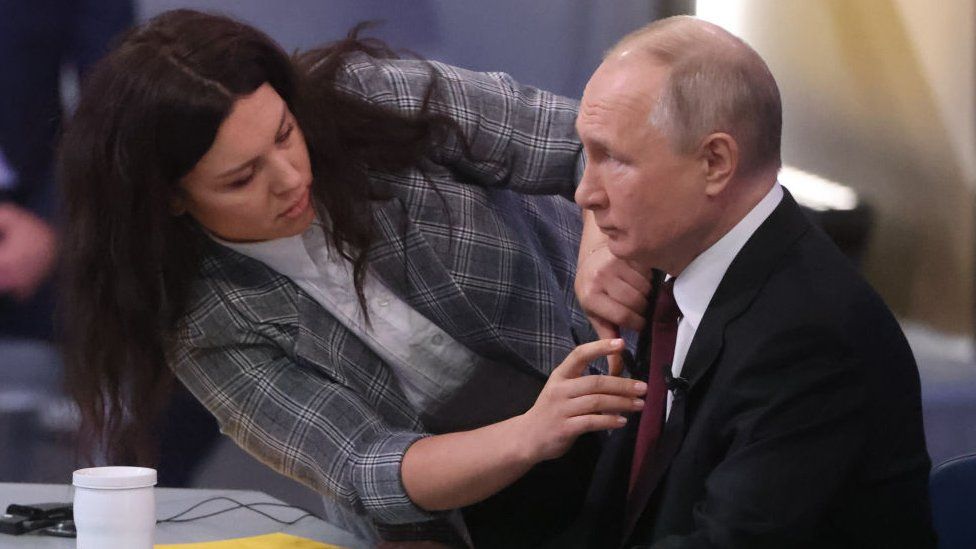 An assistant helps fix Russian President Vladimir Putin's mic