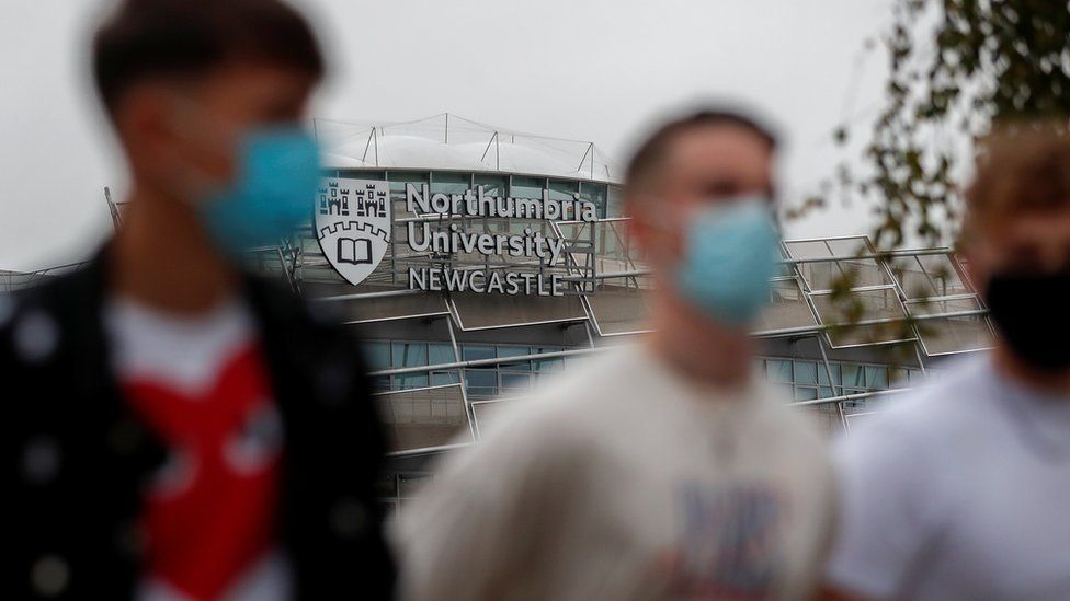 Students wearing masks walk past a Northumbria University building
