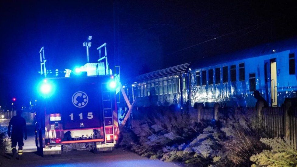 A photo at night shows a fire truck with blue lights next to a train