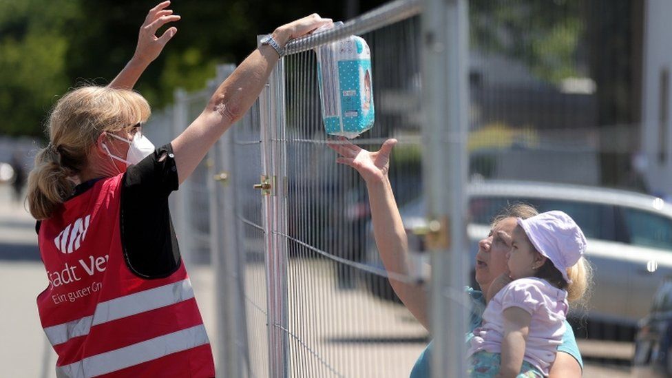A worker hands nappies over a fence to a person in quarantine in the German city of Guetersloh, June 2020