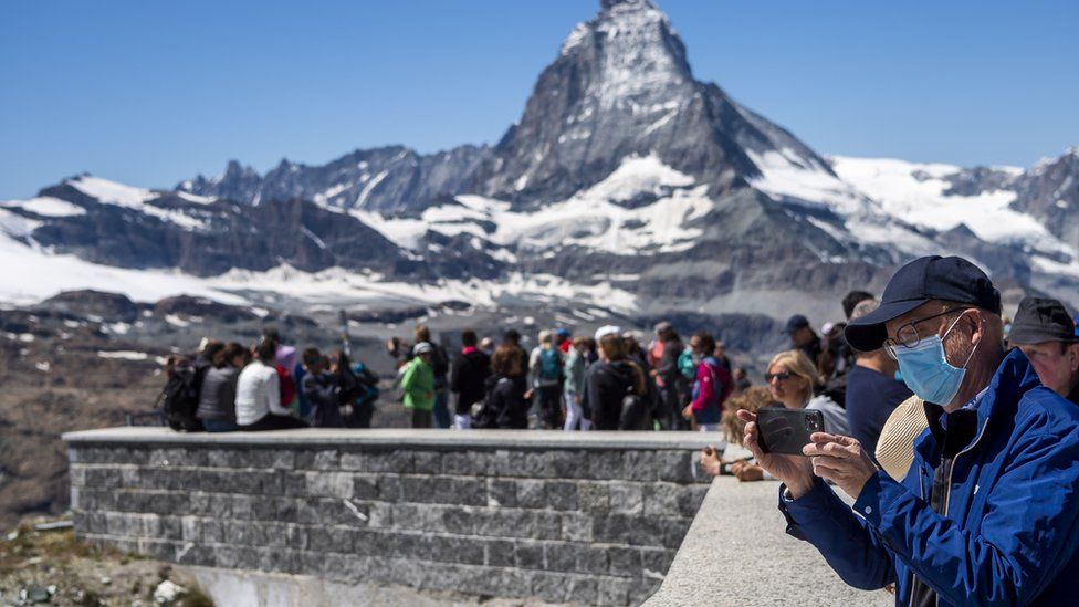 Tourist wearing a protective face mask takes a picture in front of the Matterhorn