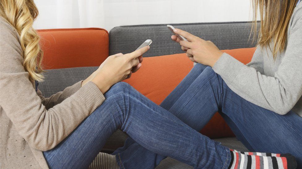 Two teenage girls with phones on the sofa