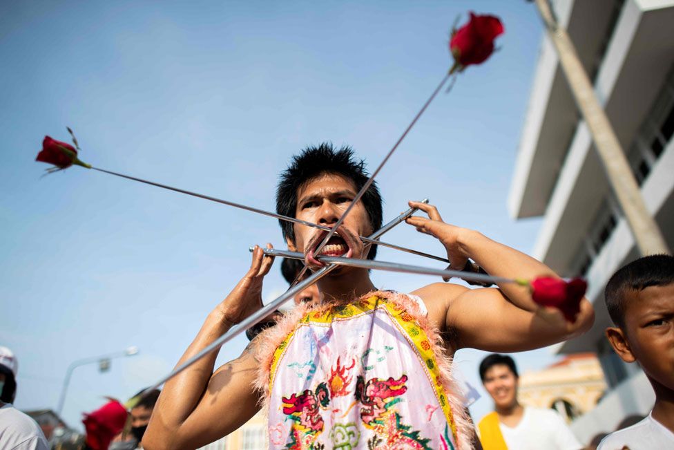A devotee of the Loem Hu Thai Su shrine has a metal rods with roses pierced through his cheeks as he parades during the annual