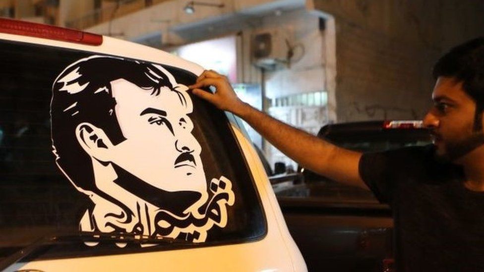 Doha man puts on a car a sticker portraying Qatar's Emir Sheikh Tamim bin Hamad Al-Thani