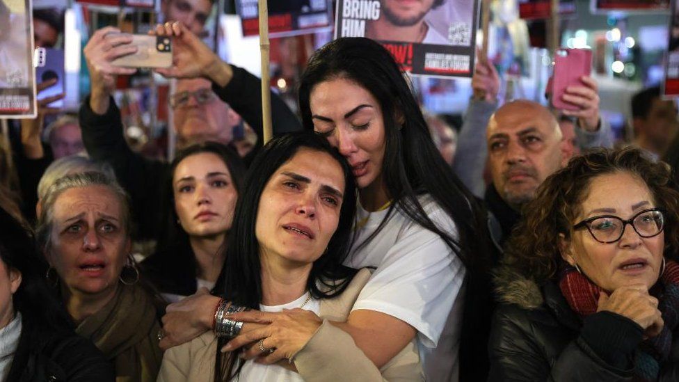 Supporters and families react as others hold pictures of hostages held by Hamas in Gaza take part in rally in Tel Aviv