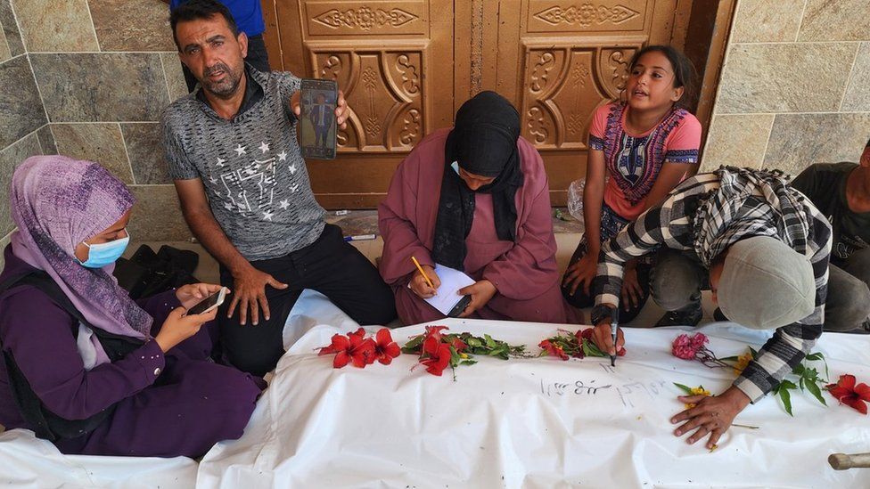 A Palestinian man holds up a photo of a dead relative whose body was found in the courtyard of Nasser hospital, in the southern Gaza Strip (24 April 2024)