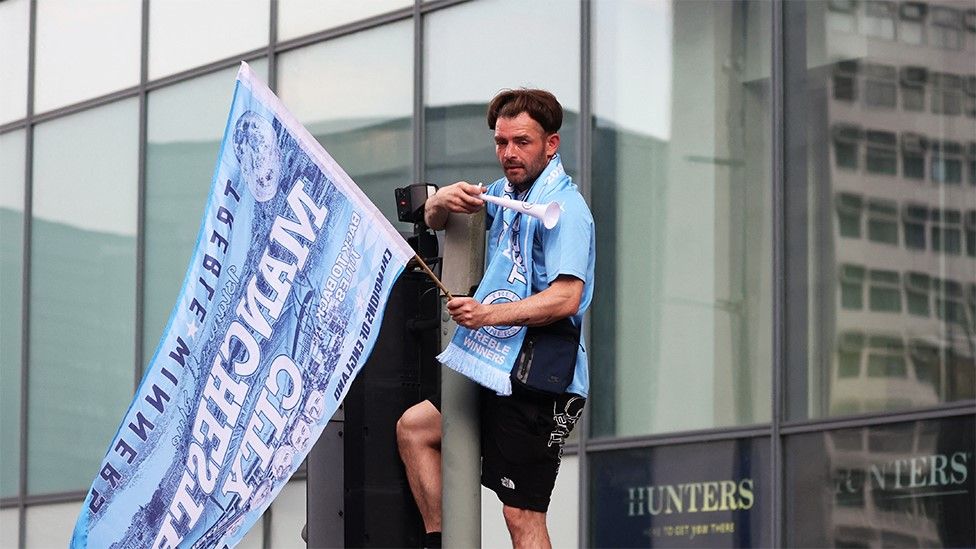 Manchester City fan sitting on a traffic light with a flag