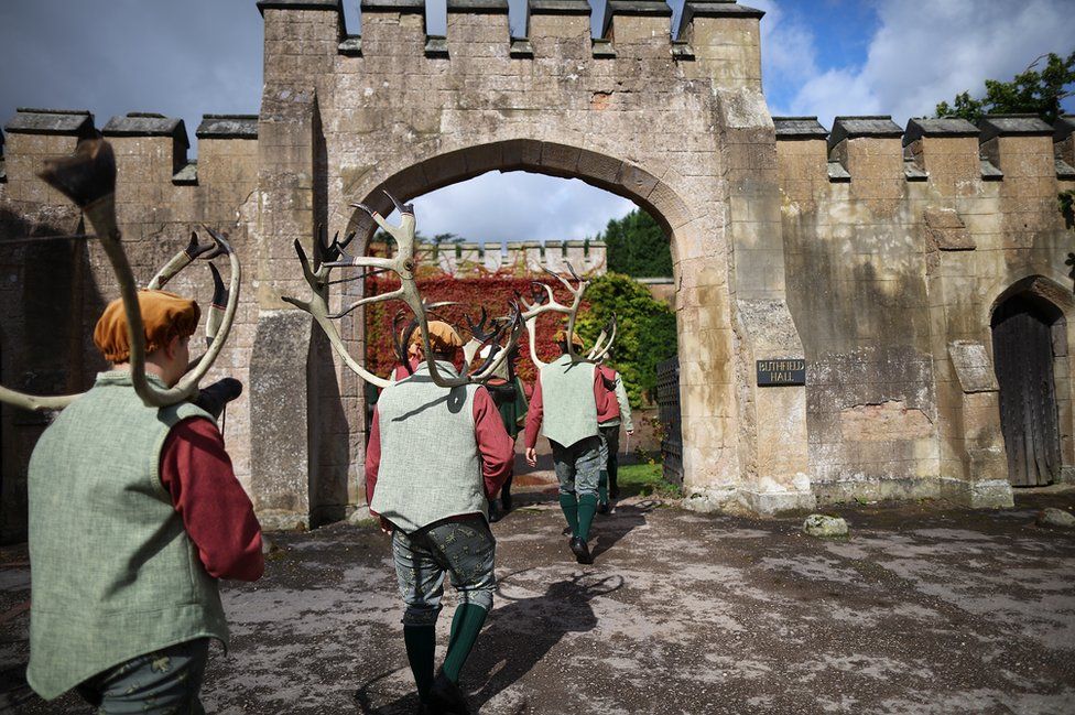 Men holding antlers walk through an arch.