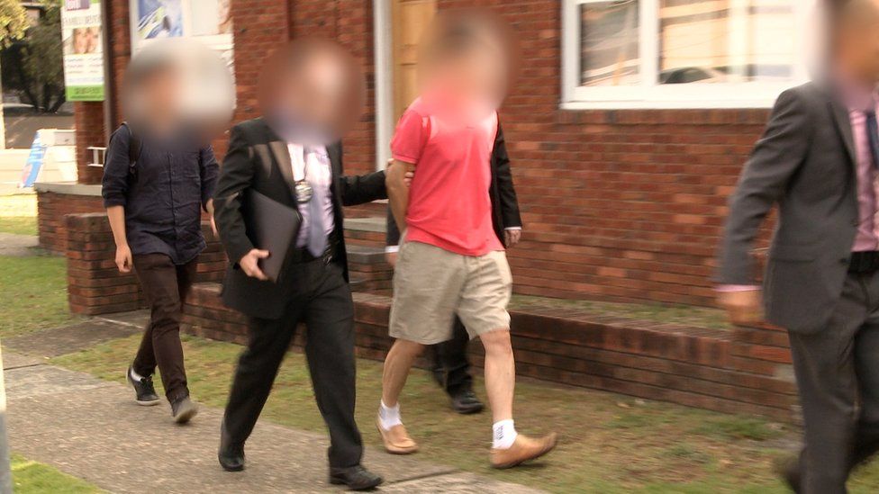 A man with a blurred face is led away by police officers following his arrest