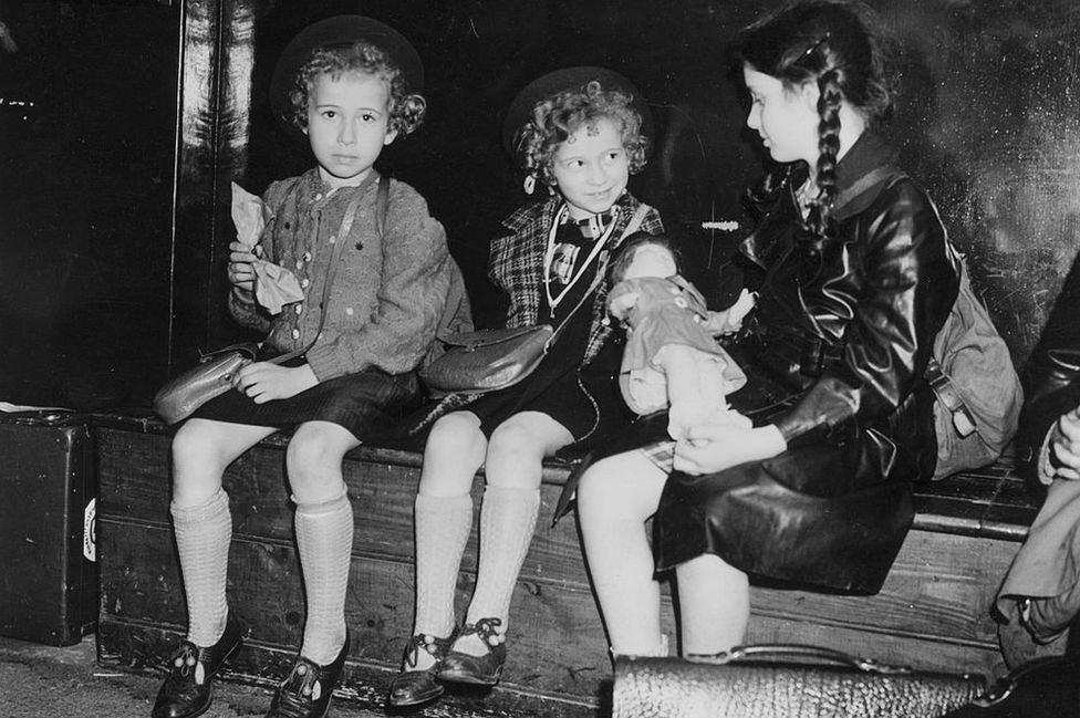 Black and white images of three young Jewish girls sitting on a station platform