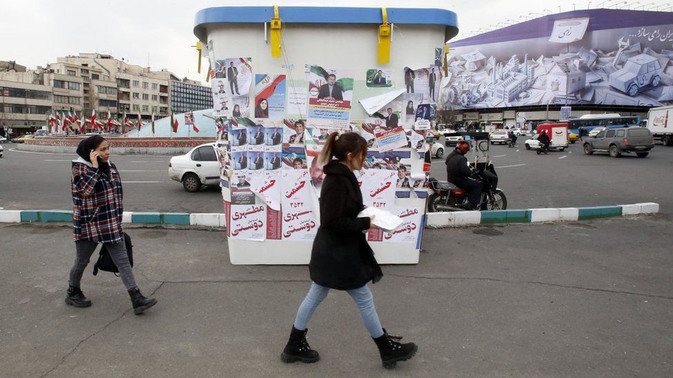 Women walk past posters of election candidates on a giant model ballot box in Tehran, Iran (28 February 2024)