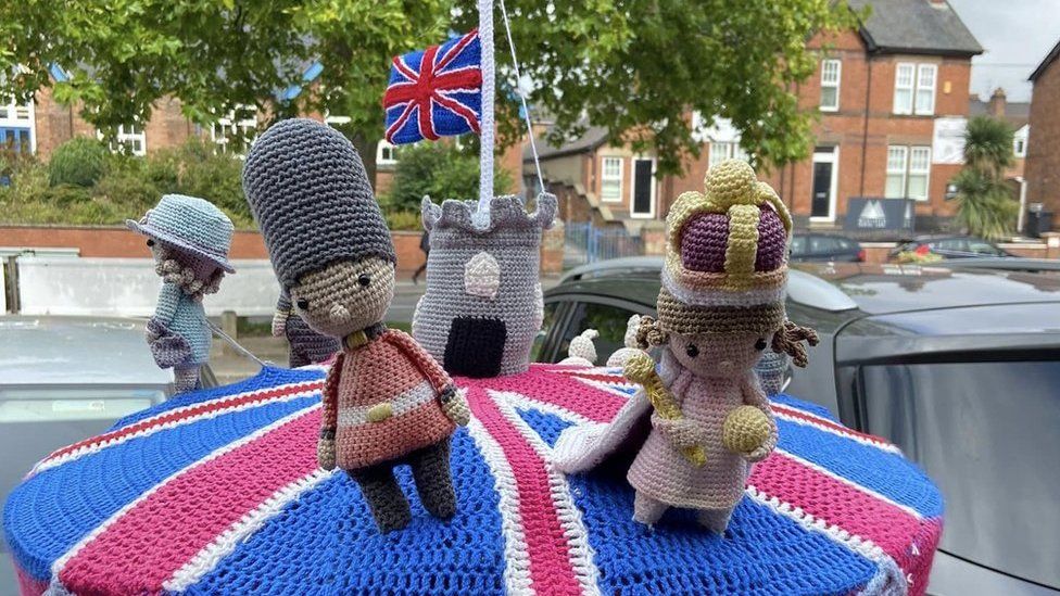 A knitted post box topper of the Queen Elizabeth II with a flag flown at half mast in Mickleover, Derby