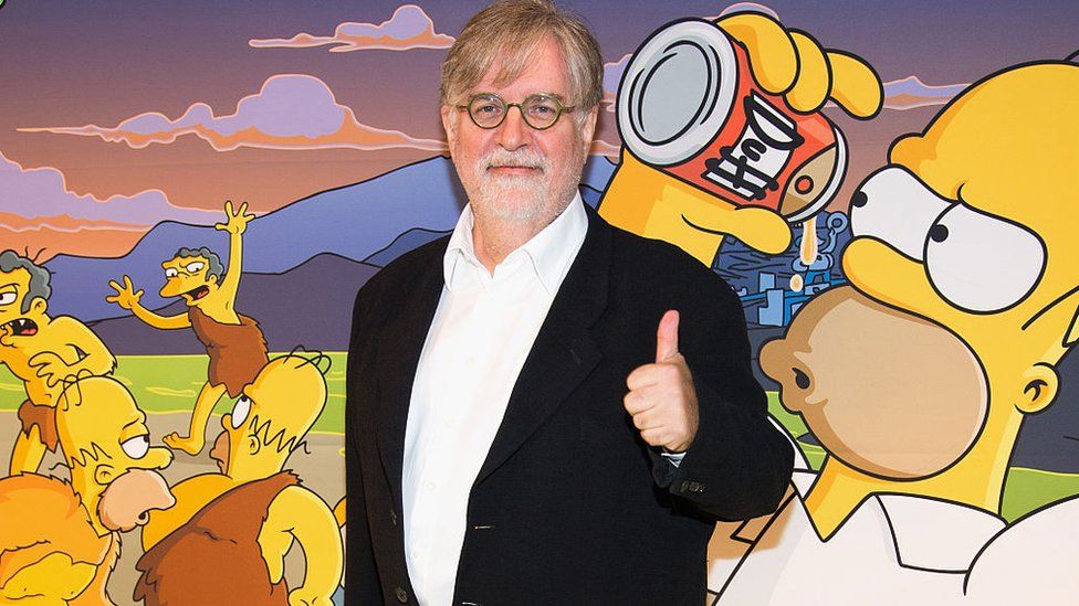 Matt Groening stands in front of a picture of Homer Simpson