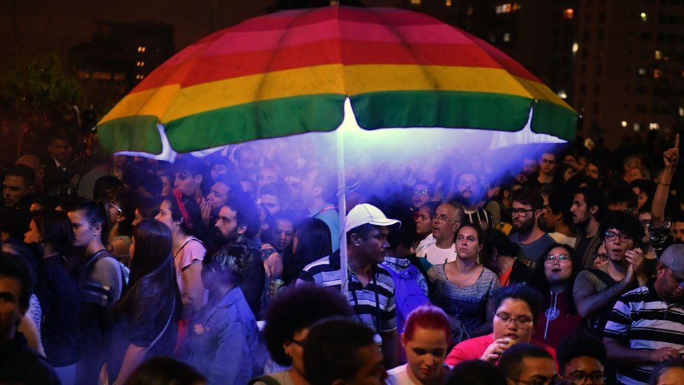 A man holds a rainbow umbrella in a big crowd at an anti-Bolsonaro protest in Sao Paulo on 10 October