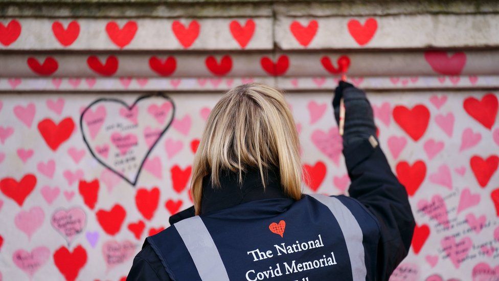 A volunteer from the Covid-19 Bereaved Families for Justice campaign group paints a heart on the National Covid Memorial Wall opposite the Palace of Westminster in central London,