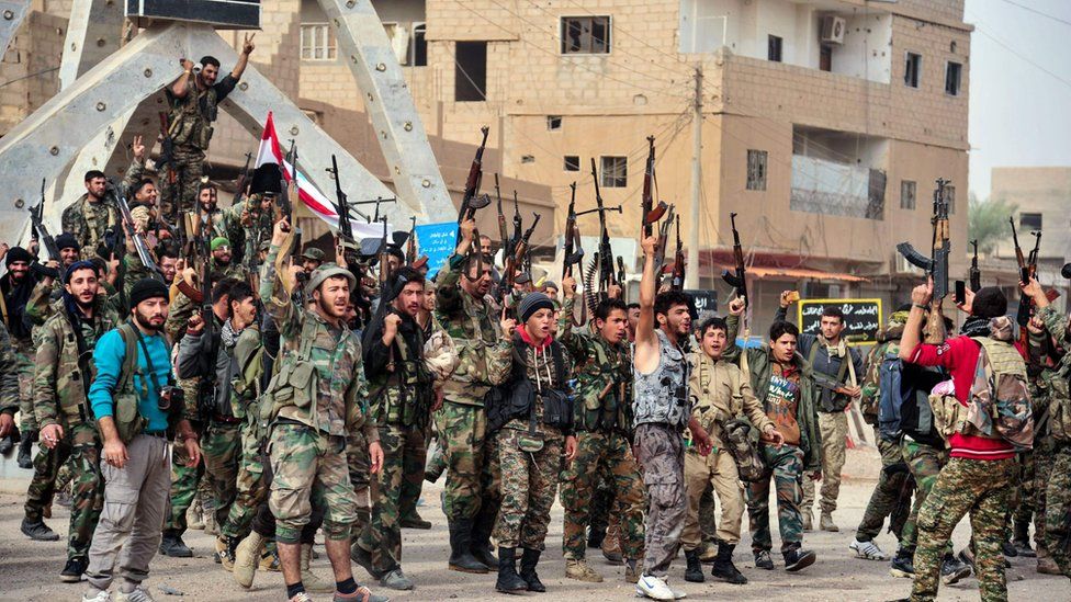 Pro-Syrian government forces gather in a public square in the Syrian border town of Albu Kamal.