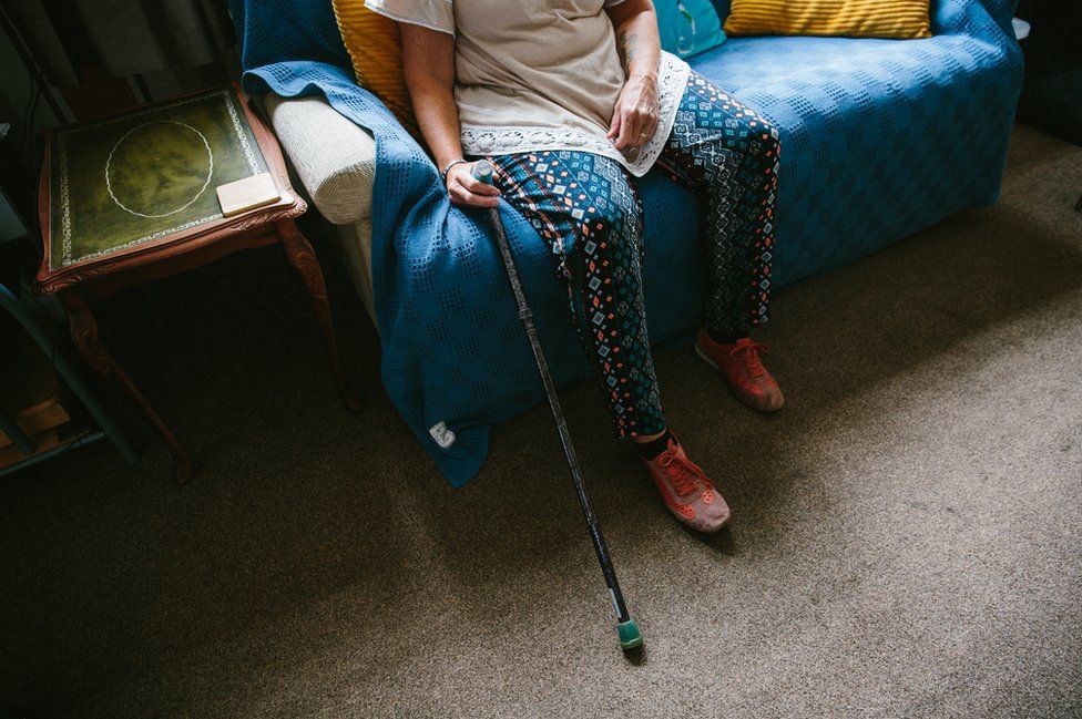 Jackie Cheetham sits at home with her walking stick