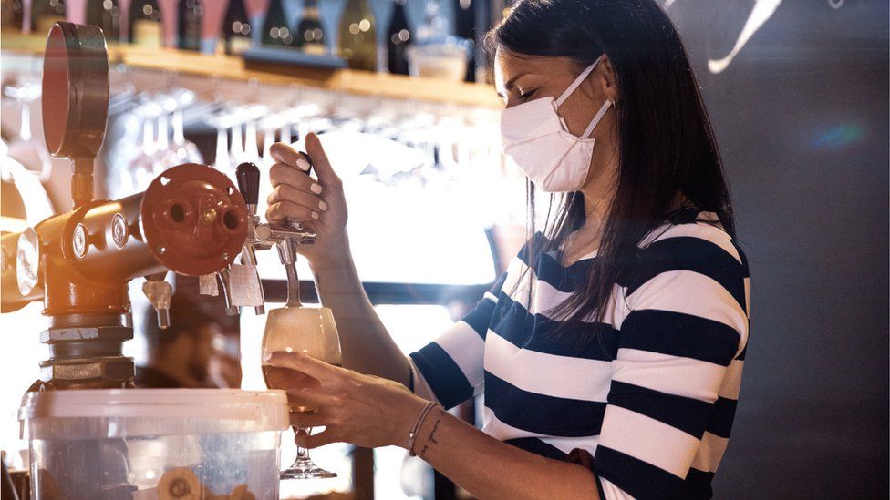 A woman pulling a pint wearing a mask