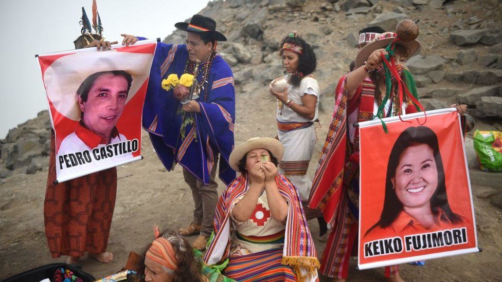 Shamans hold posters of presidential candidates Pedro Castillo (L) and Keiko Fujimori as they perform a ritual to predict the winner of the upcoming Peruvian run-off election, at San Cristobal Hill in Lima on 26 May 2021.