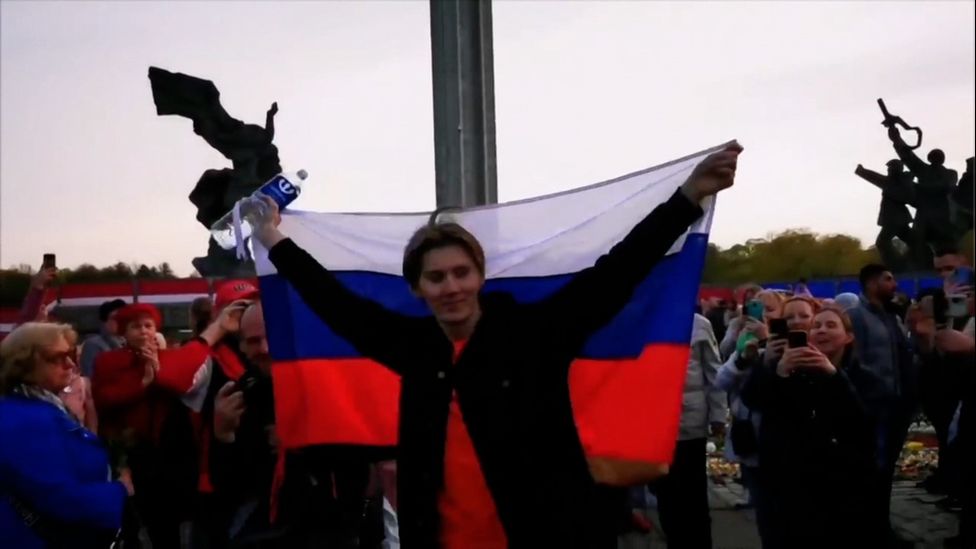 Alexander Dubyako agita uma bandeira russa para a multidão reunida em frente ao memorial de guerra de Riga em 10 de maio de 2022