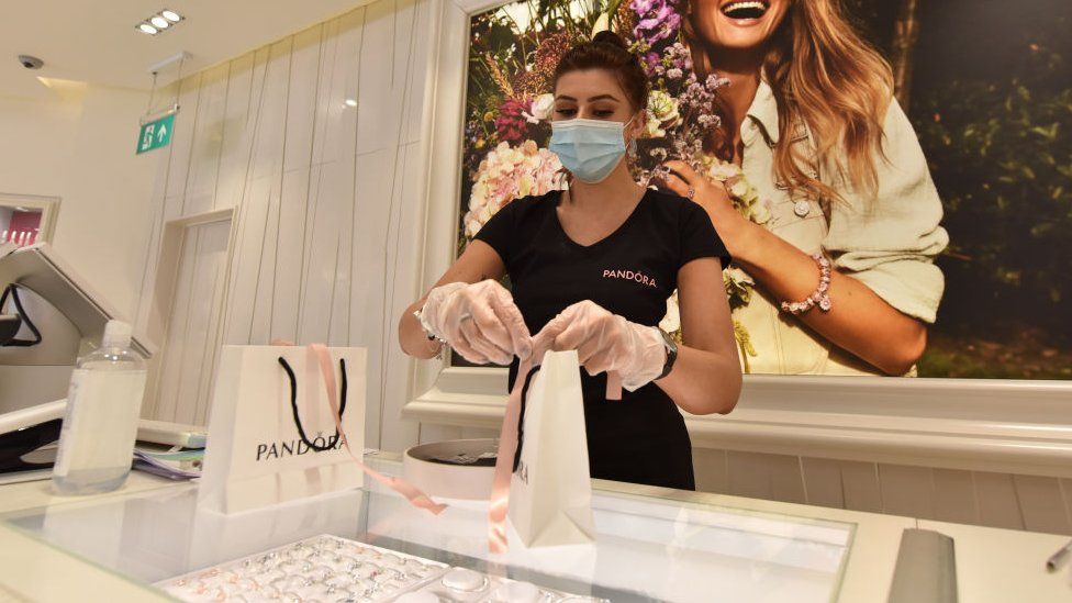 A shop assistant wearing gloves and face mask serves a customer in a Pandora store in Southend, UK