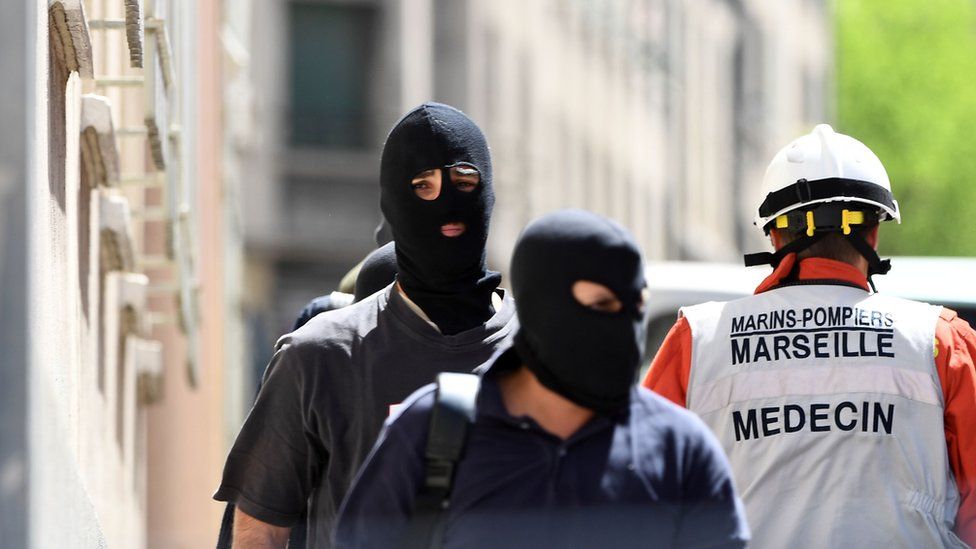 Members of the French Judiciary Police (PJ) and a naval firefighter leave after a police search at the home of one of the two men arrested in Marseille