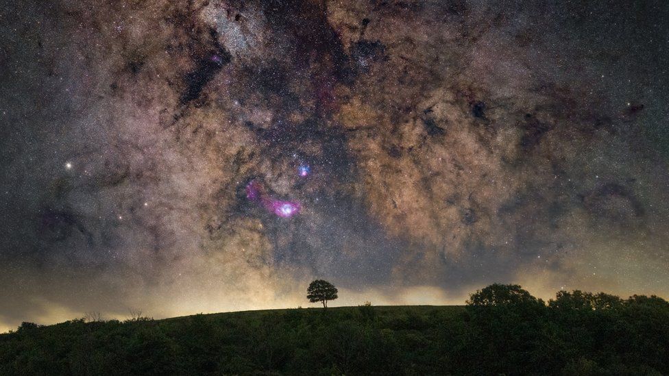 A night sky above Cissbury Ring with flashes of purple and blue among the stars