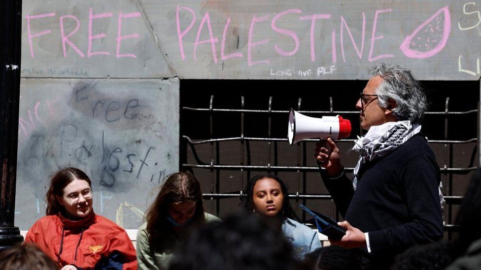A man with a speaker phone addresses students on a sit-in in an alley on the campus of Emerson College