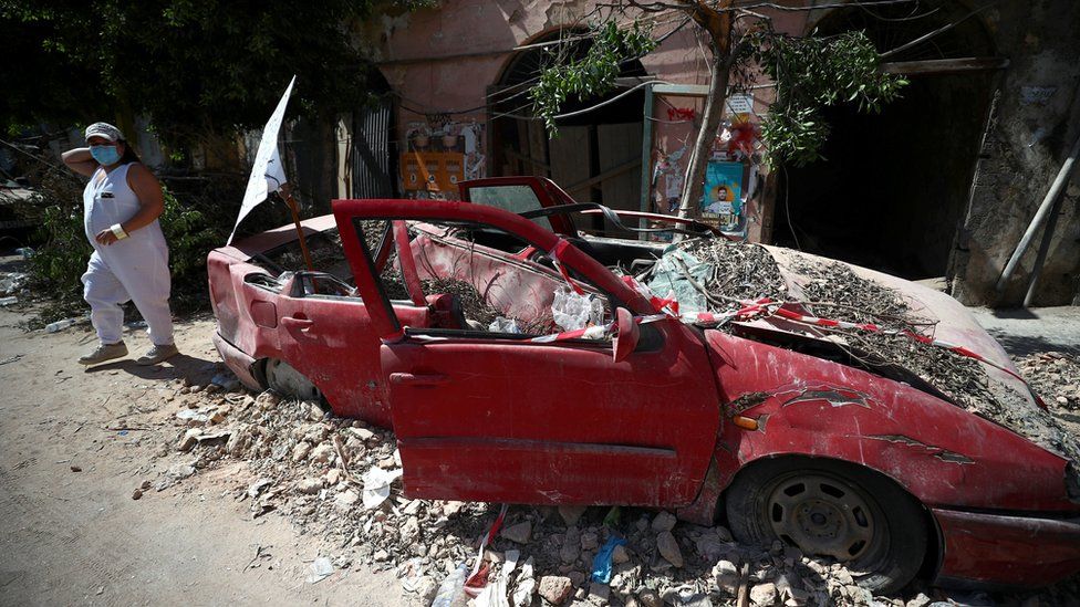 A woman walks past a damaged car following the explosion in Beirut's port area (9 August 2020)