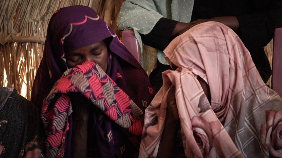 Women wipe their eyes with their hijabs during meeting in refugee camp