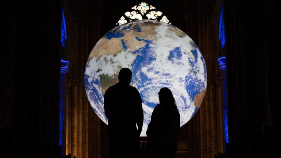 Visitors silhouetted against the illuminated globe of earth