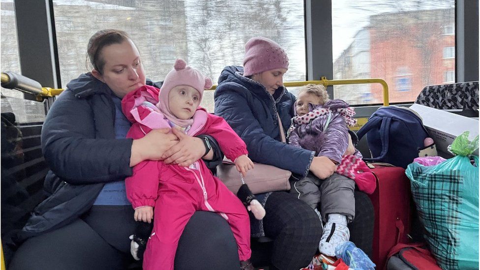Carers comfort Ukrainian children on a bus heading towards the Polish border